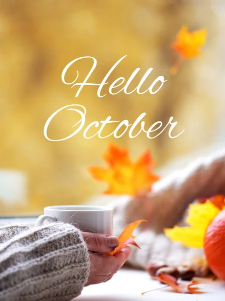 Merhaba October. Kadın eli, sonbahar penceresinde örülmüş bir fincan çay ya da kahvenin içinde güzel sonbahar yaprakları olan bir fincan kahve tutar.