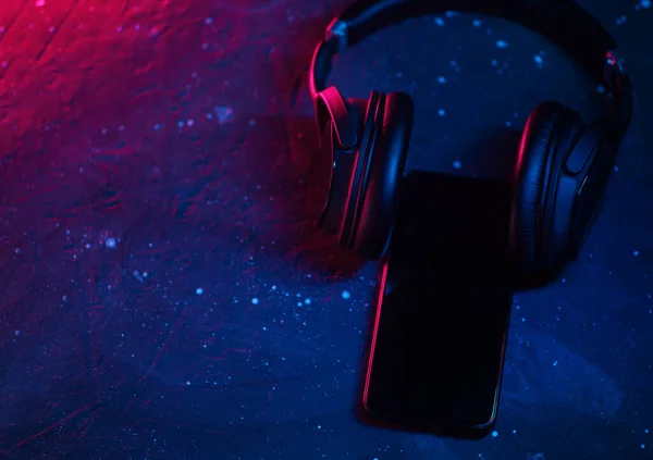 Wireless over-ear headphones on the desk, neon style. Empty smartphone with space for text