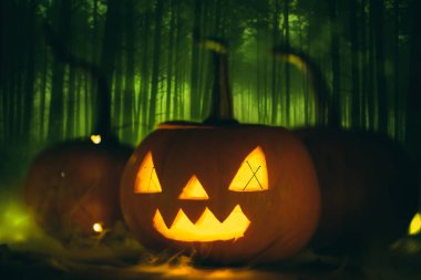 Cadılar Bayramı balkabağı oyması, arka planda tüyler ürpertici bir orman yeşil bir sis. Tatil onuruna bir partiye davetiye.