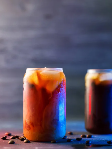 cold brew cold coffee in tall glasses with cream and roasted coffee beans. neon style backlight background