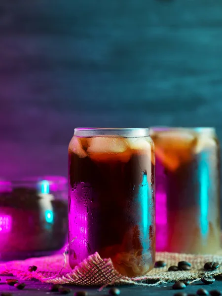 cold brew cold coffee in tall glasses with cream and roasted coffee beans. neon style backlight background