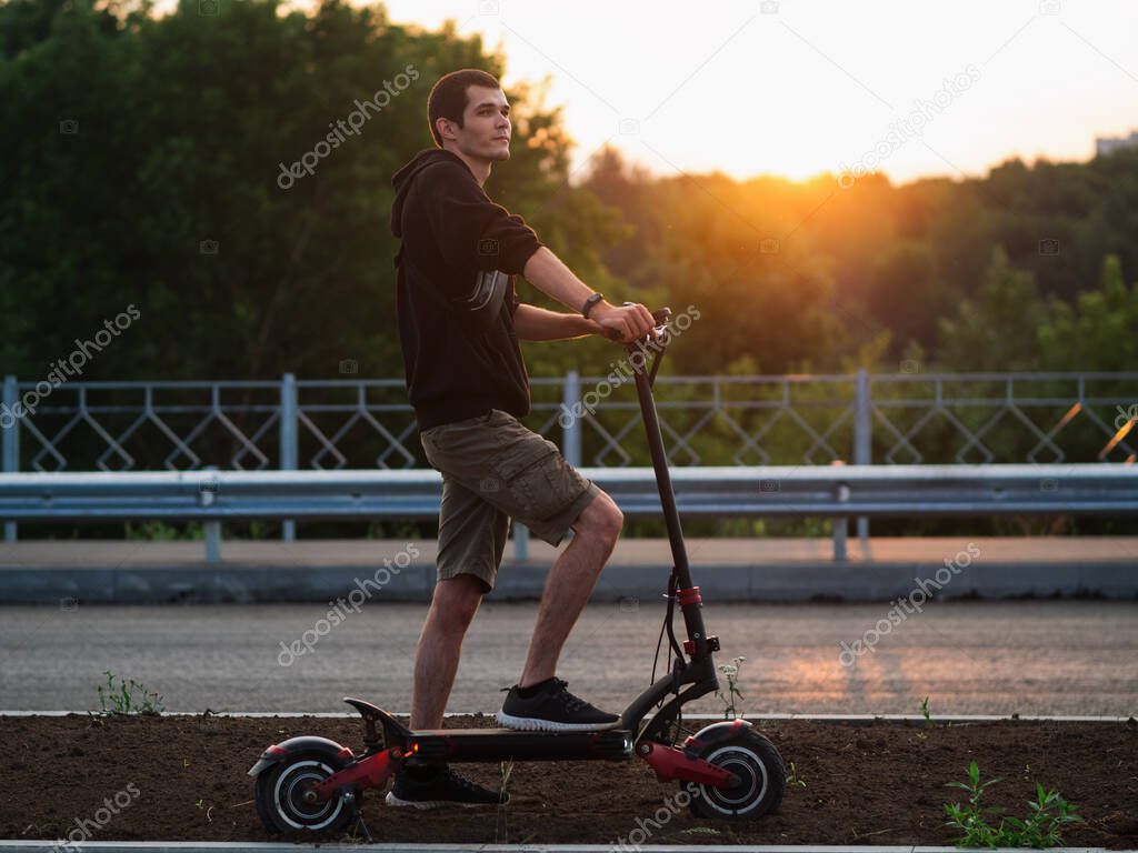 A young man on an electric scooter. Riding on the road in summer