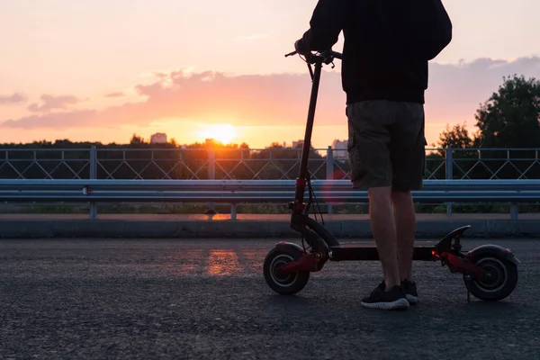 Elektrikli Scooterlı Genç Bir Adam Yolda Günbatımının Arka Planında Geleceğin — Stok fotoğraf