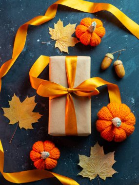 Cadılar Bayramı indirimi ya da Şükran Günü için hediye kutusu. Akçaağaç yaprakları ve balkabaklarıyla dolu karanlık bir masada turuncu kurdeleli bir hediye.