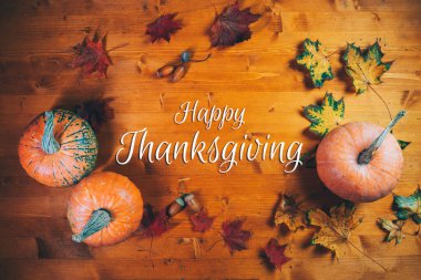 Mutlu Şükran Günü tebrikleri, ahşap masa kabakları, sonbahar yaprakları ve meşe palamudu manzarası.