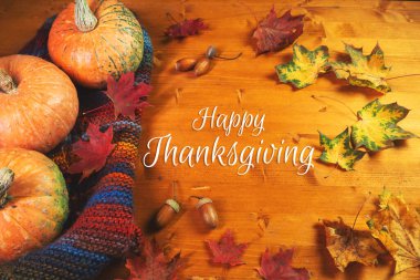 Mutlu Şükran Günü tebrikleri, ahşap masa kabakları, sonbahar yaprakları ve meşe palamudu manzarası.