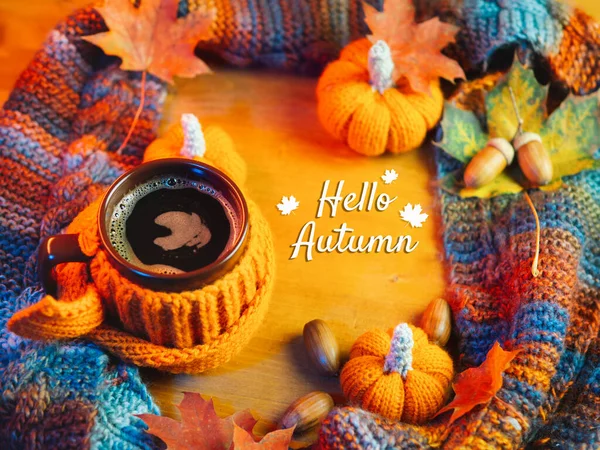 Renkli sonbahar kompozisyonu Merhaba Autumn. Bir fincan sıcak kahve örülmüş turuncu bir kazak, sıcak bir eşarp, akçaağaç yaprakları, meşe palamudu ve örülmüş balkabağı.
