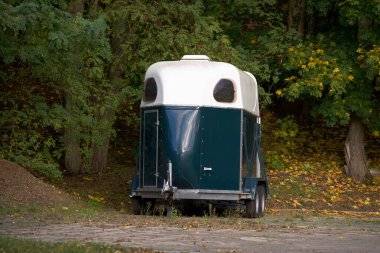 Ağaçların arkasında duran bir at römorku..