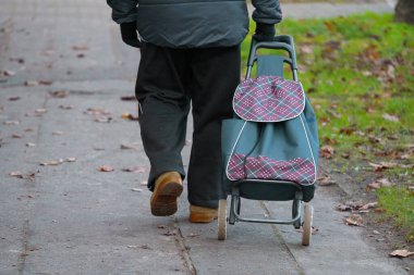 Sokakta yürüyen yaşlı bir adam alışveriş arabasını çekiyor..