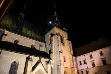 Antik gotik bir kilisenin heybetli taş cephesi gece karanlığına karşı sıcak ışıkla yıkanır.