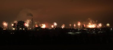 Geniş açı, karanlık, puslu gökyüzüne karşı muhteşem bir havai fişek gösterisiyle şehrin şenlikli atmosferini yakalıyor.