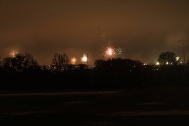 Karanlık gökyüzünde ışık patlamaları meydana geldi. Gölgeli bir şehir manzarası ve çıplak ağaçların üzerinde geceyi canlı renklerle boyadılar.