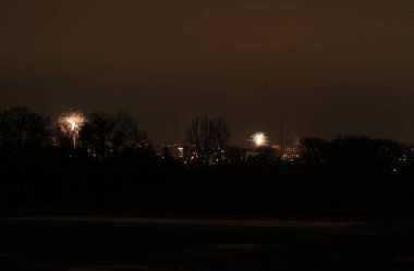 Karanlık, ağaçlarla kaplı bir ufkun üzerinde ışık patlamaları. Şehir ışıkları yanıp sönüyor.
