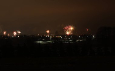 Uzak bir şehir manzarasında muhteşem havai fişekler patlıyor, gece gökyüzünü renk ve ışık patlamalarıyla boyuyor.