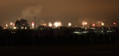 Geceleri gökyüzünde binaların ve ağaçların üzerinde sayısız havai fişeğin patladığı bir şehrin panoramik görüntüsü.