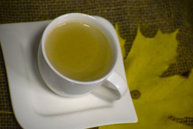 Yanında sarı bir sonbahar yaprağı olan dokulu bir yüzey üzerinde çay bardağı.