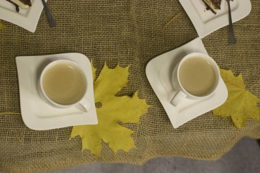 Çuval bezi masasında yaprak şeklinde çay tabakları ve yanında büyük sarı bir akçaağaç yaprağı olan iki fincan.