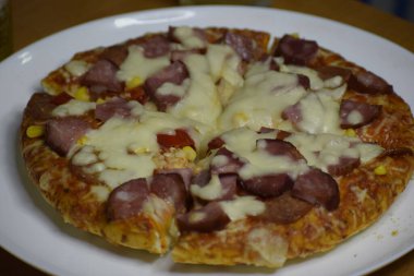 Görüntü, pizza dilimlerini beyaz tabakta çeşitli malzemelerle dilimleyip iştah açıcı bir kompozisyon oluştururken gösteriyor.