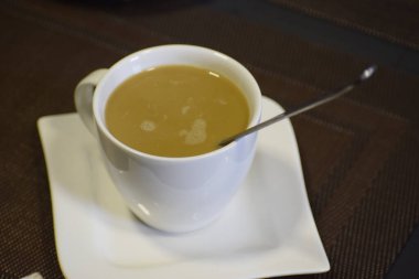 Sütlü bir fincan kahve, çay tabağına konur. İçki sıcak bir atmosfer yaratıyor. Tadı ve sabah ilhamı..