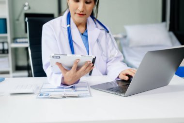 Güzel hekim doktor ofis hastanesinde masada oturuyor. Çekici terapist kadın eczacı gülümseme ve tablet ve dizüstü bilgisayar. Başarıdan sonra tedavi çalışmaları