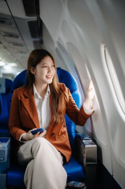 Uçakta bir koltukta oturan ve pencereden dışarı bakan Asyalı kadın seyahate çıkıyor..