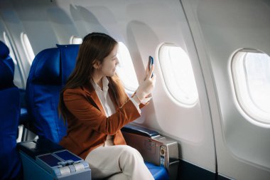 Uçakta bir koltukta oturan ve pencereden dışarı bakan Asyalı kadın seyahate çıkıyor..