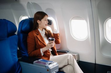 Uçakta bir koltukta oturan ve pencereden dışarı bakan Asyalı kadın seyahate çıkıyor..