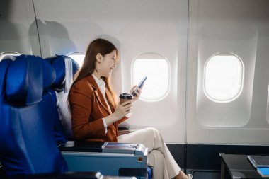Uçakta bir koltukta oturan ve pencereden dışarı bakan Asyalı kadın seyahate çıkıyor..