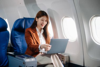 Uçakta bir koltukta oturan ve pencereden dışarı bakan Asyalı kadın seyahate çıkıyor..