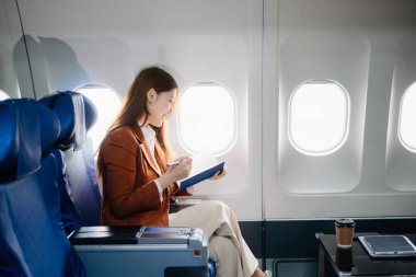 Uçakta bir koltukta oturan ve pencereden dışarı bakan Asyalı kadın seyahate çıkıyor..