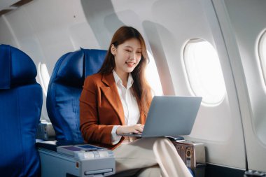 Uçakta bir koltukta oturan ve pencereden dışarı bakan Asyalı kadın seyahate çıkıyor..