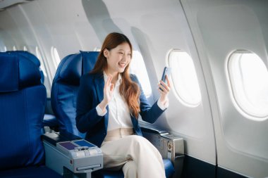 Uçakta bir koltukta oturan ve pencereden dışarı bakan Asyalı kadın seyahate çıkıyor.