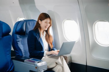 Uçakta bir koltukta oturan ve pencereden dışarı bakan Asyalı kadın seyahate çıkıyor.