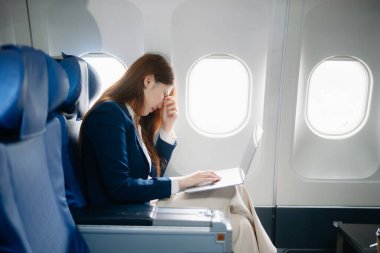 Uçakta bir koltukta oturan ve pencereden dışarı bakan Asyalı kadın seyahate çıkıyor.