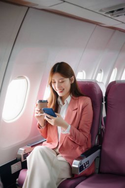 Uçakta bir koltukta oturan ve pencereden dışarı bakan Asyalı kadın seyahate çıkıyor.