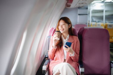 Uçakta bir koltukta oturan ve pencereden dışarı bakan Asyalı kadın seyahate çıkıyor.