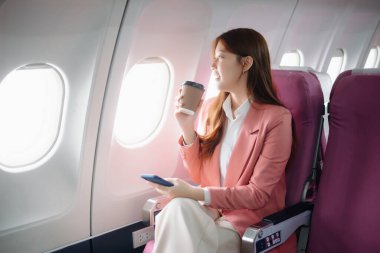 Uçakta bir koltukta oturan ve pencereden dışarı bakan Asyalı kadın seyahate çıkıyor..