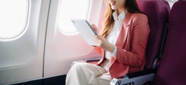 Uçakta bir koltukta oturan ve pencereden dışarı bakan Asyalı kadın seyahate çıkıyor..