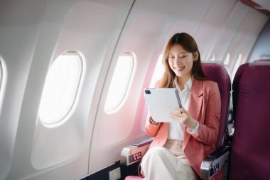 Uçakta bir koltukta oturan ve pencereden dışarı bakan Asyalı kadın seyahate çıkıyor..