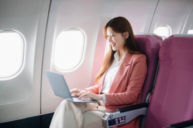 Uçakta bir koltukta oturan ve pencereden dışarı bakan Asyalı kadın seyahate çıkıyor..