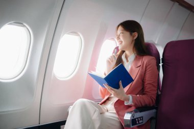 Uçakta bir koltukta oturan ve pencereden dışarı bakan Asyalı kadın seyahate çıkıyor..