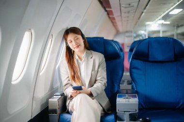 Uçakta bir koltukta oturan ve pencereden dışarı bakan Asyalı kadın seyahate çıkıyor..