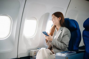 Uçakta bir koltukta oturan ve pencereden dışarı bakan Asyalı kadın seyahate çıkıyor..