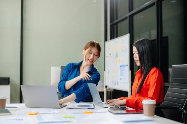 Modern ofis bünyesinde takım çalışması ve iş görüşmeleri yapan iki genç Asyalı profesyonel. 