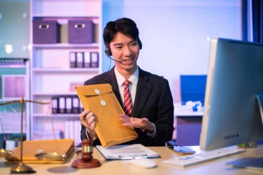 Asyalı erkek avukat müşteriyle internette sohbet ediyor, akıllı telefon dava detaylarını tartışıyor. Modern ofiste.