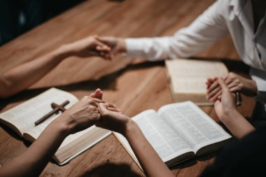 Bir grup Hıristiyan birlikte oturup odalarında açık İncil sayfaları olan ahşap bir masanın etrafında dua ediyorlar. Allah 'ın lütuf ve ihsanını dileyin.