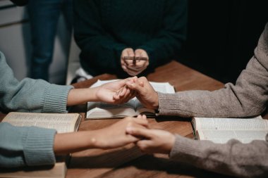 Bir grup Hıristiyan birlikte oturup odalarında açık İncil sayfaları olan ahşap bir masanın etrafında dua ediyorlar. Allah 'ın lütuf ve ihsanını dileyin.