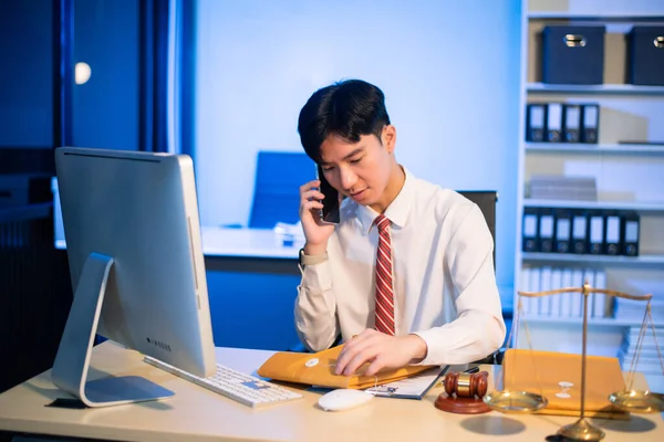 Professional young Asian lawyer at desk with legal scales and gavel, writing documents in office, offering legal services