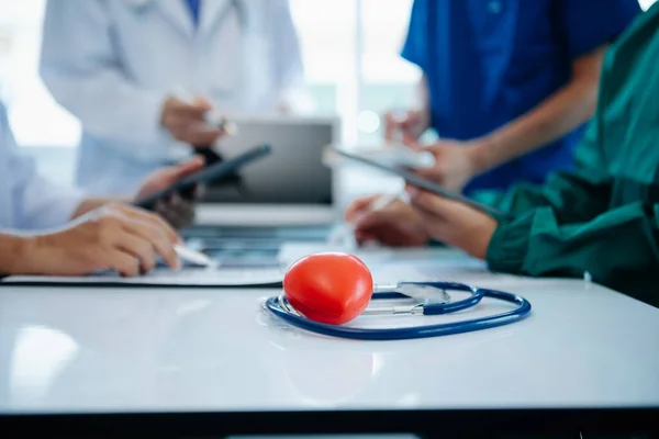 Tıbbi ekip, beyaz laboratuvar önlüklü ve ameliyat önlüklü doktorlarla toplantı yapıyor. Masada oturmuş, internette çalışan hastaları tartışıyorlar. Tıp endüstrisinde bilgisayar kullanıyorlar.