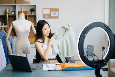 Güzel Asyalı kadın blogcu, video kaydına kamera önünde kıyafetlerini gösteriyor. 
